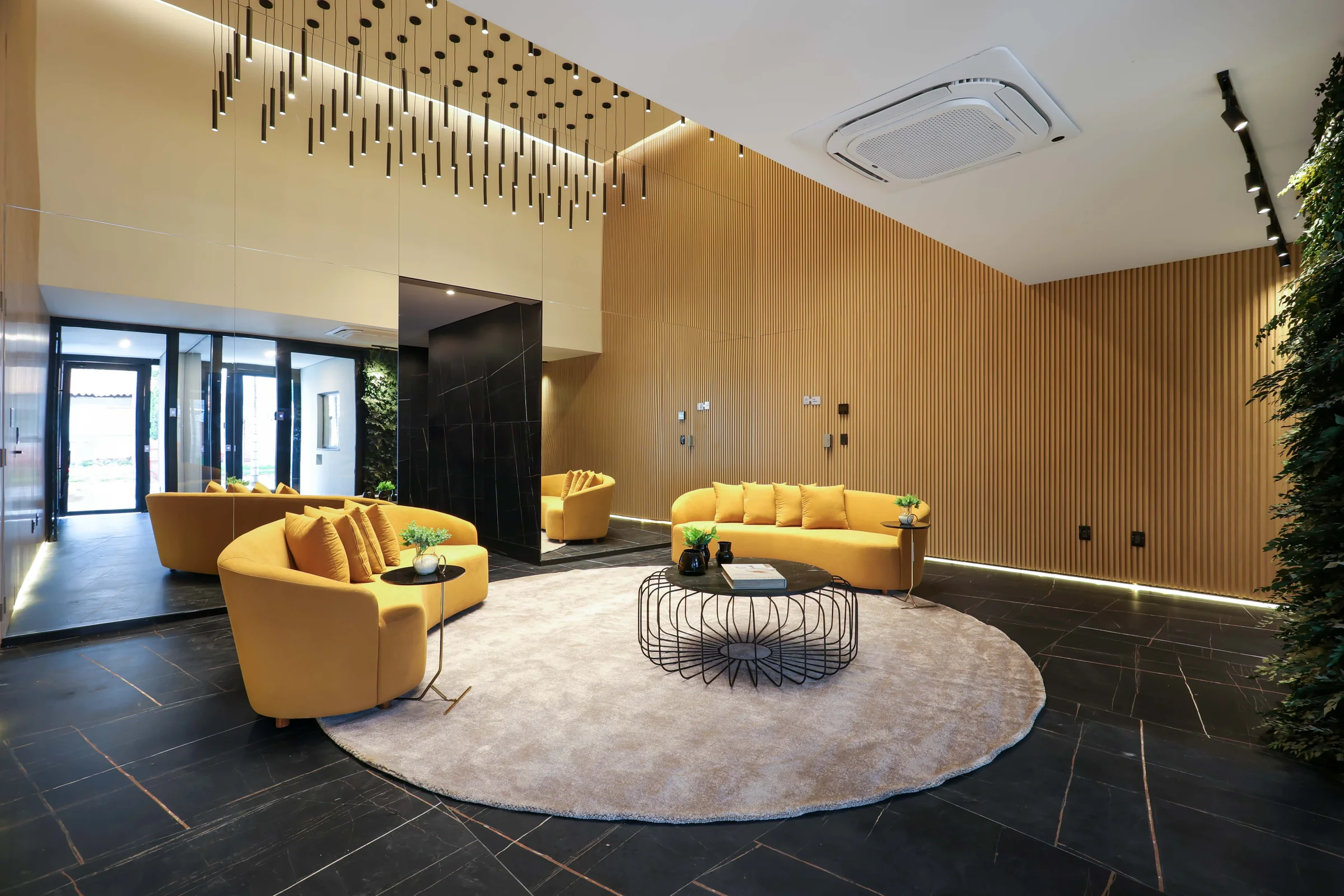 Hall social do Hub Compact Life com sofás amarelos, tapete circular e painéis de madeira
